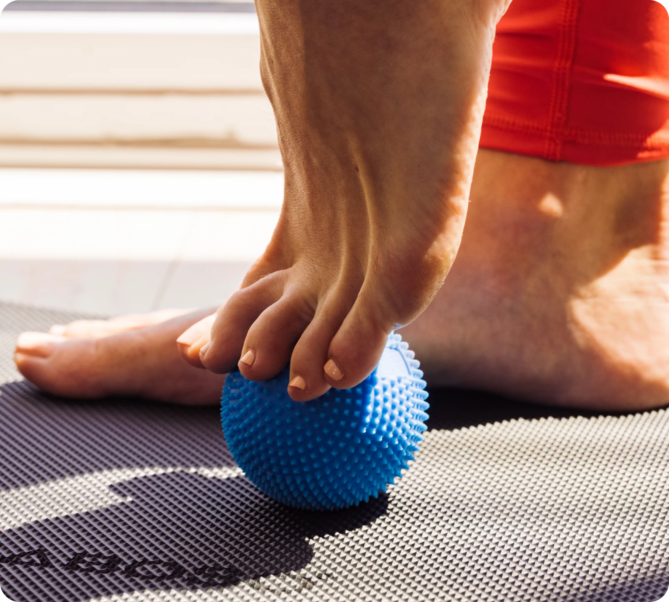 Person using a blue massage ball on a foot on a mat.